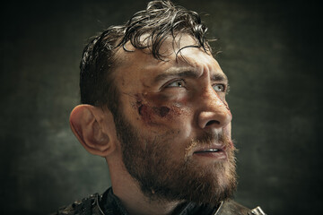Looking aside. Portrait of one brutal bearded man, medeival warrior or knight with dirty wounded face