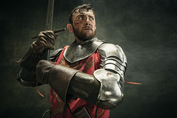 Portrait of one brutal bearded man, medeival warrior or knight with dirty wounded face holding sword