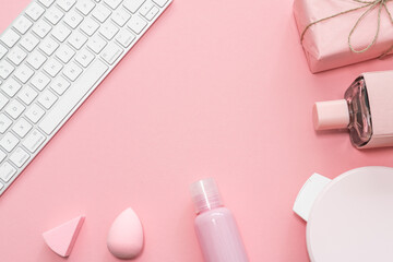 Beauty blog concept. Female make up accessories like shower gel, beauty blender, gift and modern keyboard on a pink pale background. 