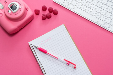 Business concept. Workspace with business accessories: keyboard, notebook and fast print camera on a pink background with berries. Girl with manicure writing in a notebook.