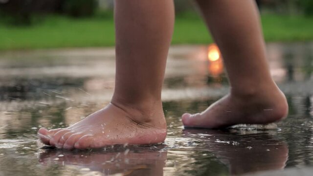 Close Up Of Legs Of Playful Baby Barefoot Stomping On Puddle On Asphalt