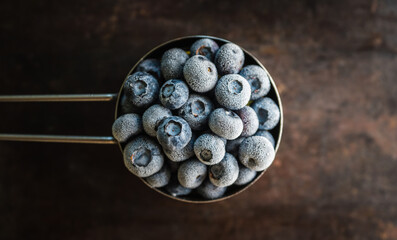 Frozen blueberries in metal cup on the rustic background. Selective focus.