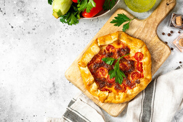 Vegetable galette with zucchini, tomatoes, sweet pepper and mozzarella on a serving board on a light gray culinary background top view from a copyspace