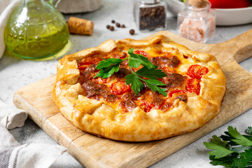 Vegetable galette with zucchini, tomatoes, sweet pepper and mozzarella on a serving board on a light gray culinary background closeup