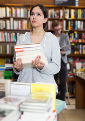 Happy female student standing in library with pile of books in hands
