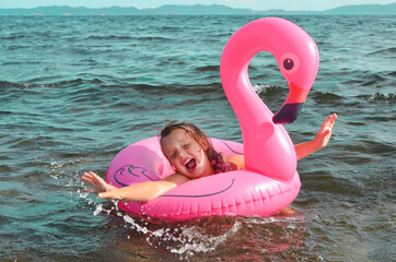happy child swimming in the splashes of water in the sea on an inflatable flamingo circle, active...