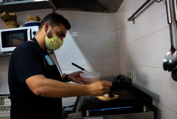 restaurant and bar cook working in the kitchen with a mask in the new normal of the covid 19 pandemic
