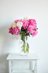 Empty white wall with pink flowers. Peonies in a glass vase in a bright interior