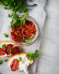 Italian cuisine. Bruschetta with dried tomatoes and cottage cheese. Italian food on a white background. Toasts are being prepared. Dried tomatoes in a jar. Baguette and ricotta