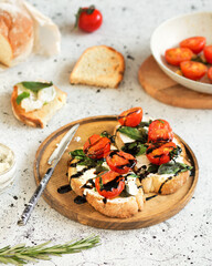 Italian cuisine. Bruschetta with baked tomatoes, basil and soft cheese. Dressing from balsamic sauce. Italian food on a white background. Toasts are being prepared. Baguette, rosemary, and ricotta.