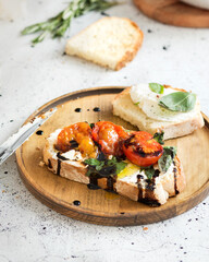 Italian cuisine. Bruschetta with baked tomatoes, basil and soft cheese. Dressing from balsamic sauce. Italian food on a white background. Toasts are being prepared. Baguette, rosemary, and ricotta.