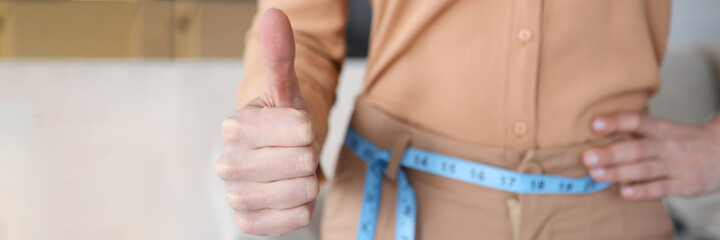 Woman with measuring tape at her waist showing thumb up closeup