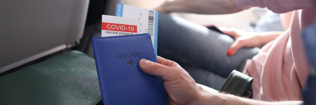 Man flying on plane and holding immunization passport against covid 19 and tickets closeup