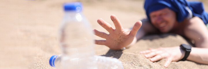 Dehydrated man crawling on sand for bottle of drinking water closeup
