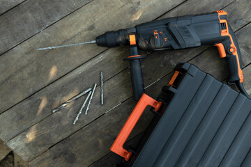 Top view of black hammer drill and box for it, steel drills on the wiiden desk.Empty space