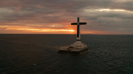 Catholic cross in sunken cemetery in the sea at sunset, aerial drone. colorful sky during the sunset. Large crucafix marking the underwater sunken cemetary, Camiguin Island Philippines.