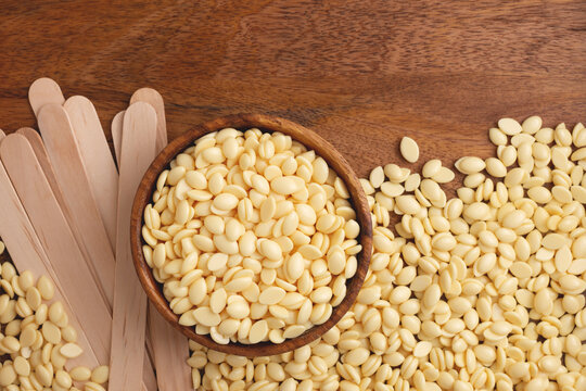 Natural hair removal wax beans in wooden bowl and wooden spatulas on wooden background with copy space.