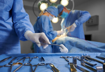 Close up of doctor hand holding forceps with tampon while surgeon and assistant performing plastic...
