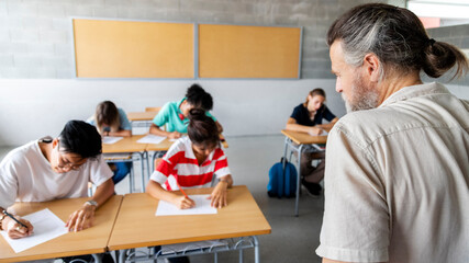 Mature caucasian adult male teacher monitors group of multiracial high school students taking an...