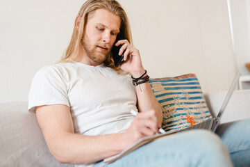 Bearded blonde man talking on cellphone while working with laptop