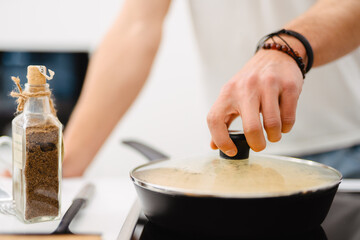 Young white man using frying pan while cooking in kitchen