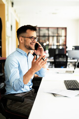 Young businessman using laptop in his office. Handsome man talking to the phone