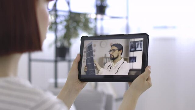 Close Up Over The Shoulder View Of Digital Tablet Screen With Professional Male Medical Practitioner Talking About Good Results Of Patient CT Scan. Woman Talking With A Doctor Online