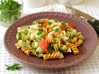 Salad of pasta. Spirals with vegetables, surimi and avocado. With leaves of basil as condiment.