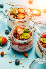 Yogurt with granola, fresh berries and nuts in a jar on a blue background. Healthy breakfast and dessert milk concept. Beautiful bright food photo
