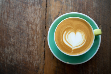 Top view of Latte coffee or cappuccino coffee in yellow cup with heart latte art on wooden table.