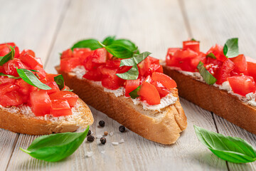 Bruschetta with tomato and basil on a light wooden background.