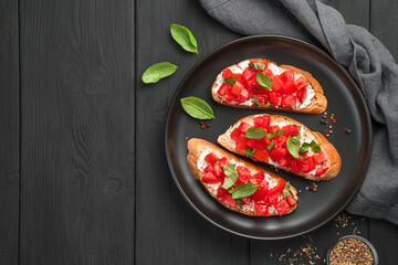 Bruschetta with tomato, butter, basil and cheese on a black background.