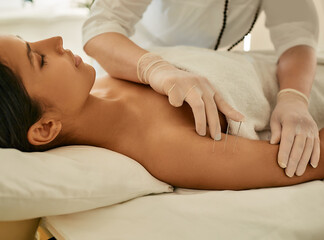 Woman patient receives body acupuncture procedure lying down in Asian wellness salon