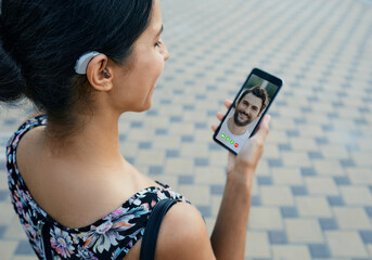 Brunette woman with a hearing aid behind the ear communicates with her boyfriend via video communication via a smartphone