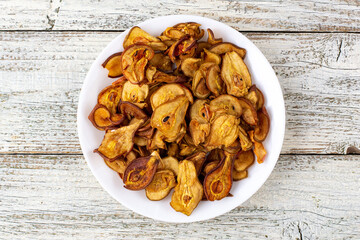 A pile of dried pears in slices on a white plate on wooden background. Dried fruit chips. Healthy food