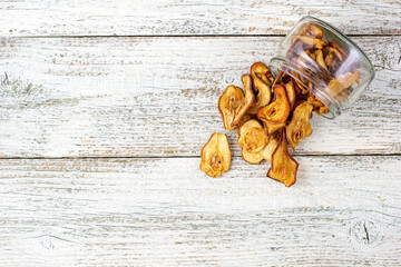 A pile of dried slices of pears pills out of a glass jar on white wooden background. Dried fruit chips. Healthy food