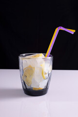 lemonade in a glass with a straw on a white table and black background. Minimalist