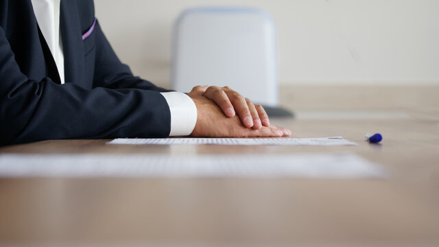 Man in an elegant suit put his hands on a wooden table next to a sheet of paper and a fountain pen. Without a face. Anonymous meeting participant: boss, official, lawyer, or businessman