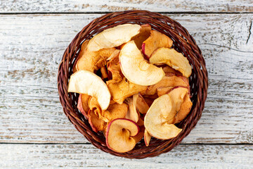 A pile of dried slices of apples in wicker basket on white wooden background. Dried fruit chips. Healthy food