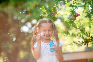 a little girl blows soap bubbles in the park