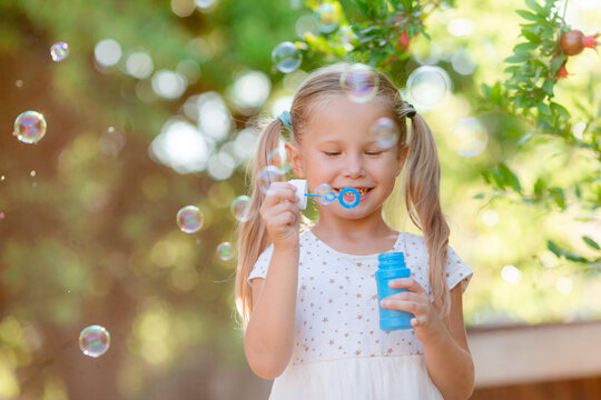  funny little blonde girl blowing soap bubbles in summer in the park
