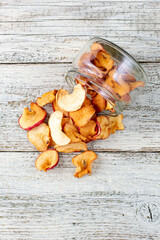 A pile of dried slices of apples pills out of a glass jar on white wooden background. Dried fruit chips. Healthy food