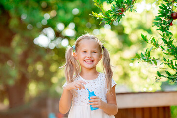 a little girl blows soap bubbles in the park