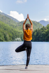 Fototapeta na wymiar Young woman doing morning yoga routine near lake.