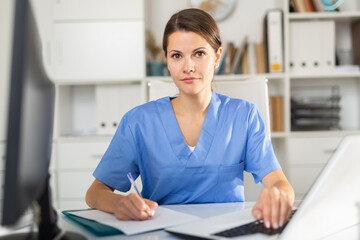 Obraz na płótnie Canvas Positive female doctor working on laptop in clinic