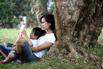 mother and son  reading a book together  in the park