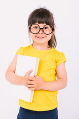 Smiling little girl wearing yellow t-shirt and round black glasses holding a book in her hands on white background