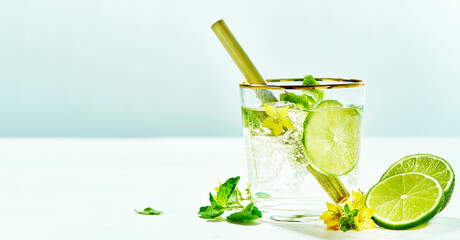 Fresh drinks with lime and mint garnishing with fresh flowers, cold summer lemonade on blue background.copy space. Modern minimalism concept. wide banner.