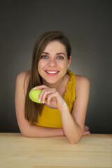 Laughing woman sits at table and hold green apple.