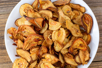 A pile of dried pears in slices on a white plate on wooden background. Dried fruit chips. Healthy food
